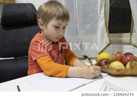 Young boy doing homework and writing on notebook at home Young boy doing homework and writing on notebook at home 126684254