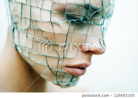 Human figure wearing a transparent cracked glass mask, symbolizing containment and immune strain, showcasing emotional depth and vulnerability in a surreal context 126685105