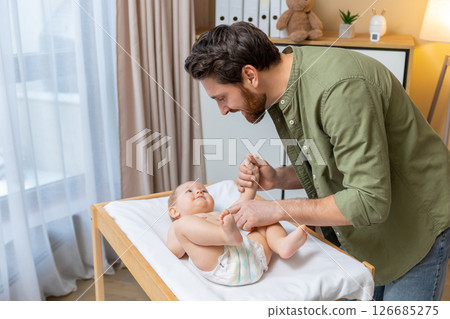 Dad changing a diaper to his little baby boy while the kid smiling and looking happy 126685275