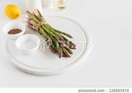 Fresh asparagus shoots with spices and lemon on white table. Top view Fresh asparagus shoots with spices and lemon on white table. Top view 126685878