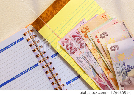 Turkish lira banknotes are placed beside planner, showcasing moment of organization finance in workspace. Turkish lira banknotes are placed beside planner, showcasing moment of organization finance in workspace. 126685994