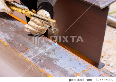 Skilled worker carefully operates cutting torch on metal beams at construction site under metalworking 126686009