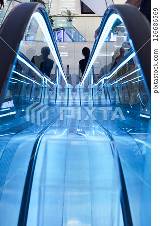 Brightly lit escalator features blue lighting in a busy shopping center. Brightly lit escalator features blue lighting in a busy shopping center. 126686569