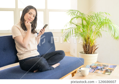 A woman sitting on a sofa and operating a smartphone A woman sitting on a sofa and operating a smartphone 126686607