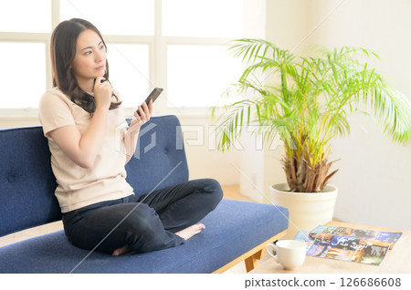 A woman sitting on a sofa and operating a smartphone 126686608