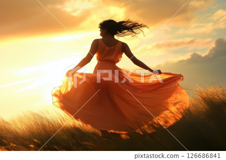 Girl twirls joyfully in a flowing dress on grassy hill under sunset rays 126686841