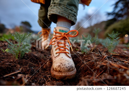Close-up of white boot stepping in garden path surrounded by green crops 126687245