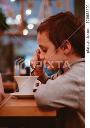 Thoughtful Boy Enjoying a Warm Beverage in Cozy Cafe Thoughtful Boy Enjoying a Warm Beverage in Cozy Cafe 126688391