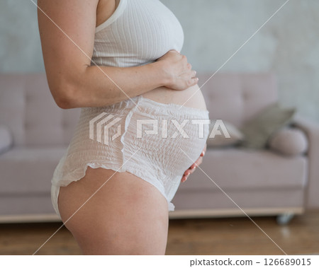 Caucasian pregnant woman in adult diapers suffers from incontinence. Close-up of belly.  126689015
