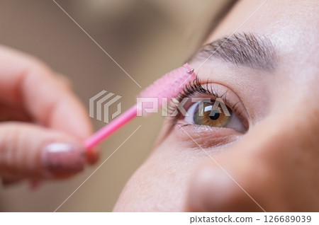 Caucasian woman brushing her eyelashes after lamination. Caucasian woman brushing her eyelashes after lamination. 126689039
