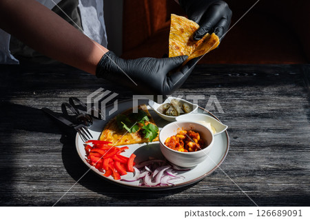 A chef wearing black gloves prepares fajitas.  126689091