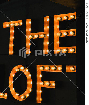 Glowing capital letters spelling The Loft emitting warm light, casting soft illumination against shadowy background, creating inviting nighttime signage atmosphere. Large illuminated letters The Loft Glowing capital letters spelling The Loft emitting warm light, casting soft illumination against shadowy background, creating inviting nighttime signage atmosphere. Large illuminated letters The Loft 126689129