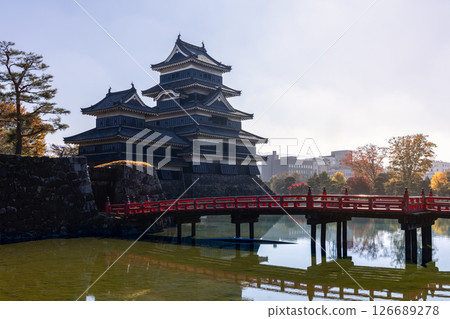 Matsumoto Castle and its red bridge reflected in the still moat water, surrounded by autumn foliage 126689278