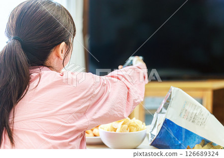 一位女士一邊吃零食一邊看電視 126689324