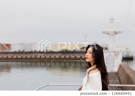 一位身穿白衣的年輕女子在港口休息 126689441