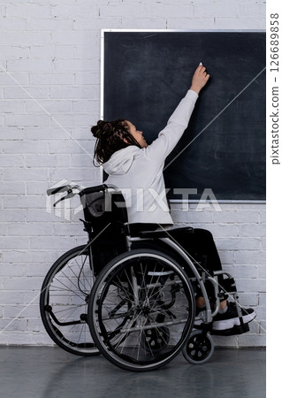 An empowered wheelchair user is writing on a chalkboard, demonstrating their desire for education 126689858