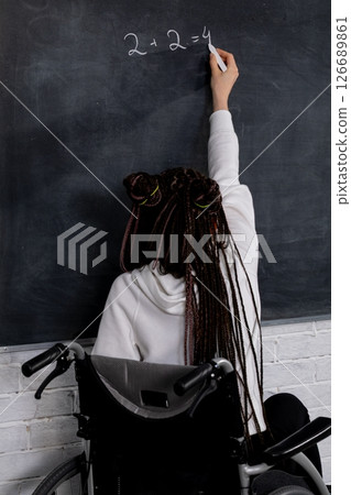 An empowered educator shares their knowledge by writing on a chalkboard while in a wheelchair An empowered educator shares their knowledge by writing on a chalkboard while in a wheelchair 126689861
