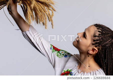 A woman dressed in beautiful traditional attire is holding a sheaf of wheat proudly 126689888