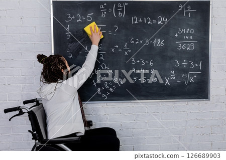 A Student in a Wheelchair Writing Mathematical Equations on a Chalkboard during Class A Student in a Wheelchair Writing Mathematical Equations on a Chalkboard during Class 126689903