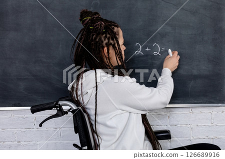 A dedicated teacher in a wheelchair inspires students while skillfully writing on a chalkboard 126689916
