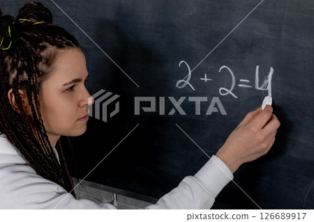 A dedicated student diligently solving a complex math equation on a chalkboard in class 126689917