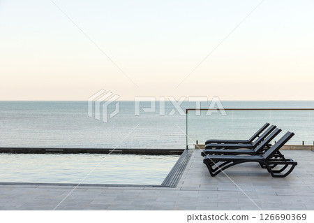 Relaxing ocean view with a modern infinity pool and lounge chairs Relaxing ocean view with a modern infinity pool and lounge chairs 126690369