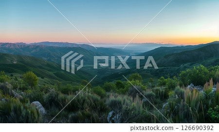 A serene valley unfolds from a mountaintop at dawn; mist weaves through trees as the world awakens. 126690392