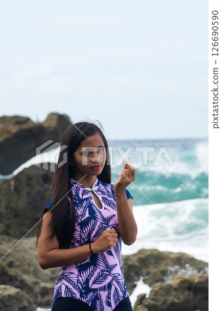 young asian woman shows off white round pebble found on pebble beach near tropical sea 126690590