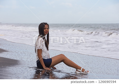 young woman sitting on wet black sand beach near waves 126690594