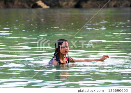 Young asian woman in swimsuit standing in tropical river with rocks behind Young asian woman in swimsuit standing in tropical river with rocks behind 126690603