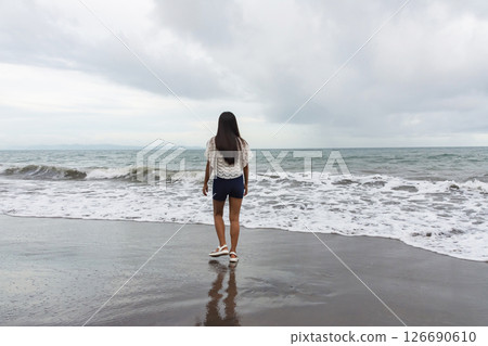 Confident young woman walking alone on the beach near the sea waves Confident young woman walking alone on the beach near the sea waves 126690610