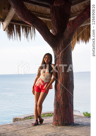 young asian woman in one piece swimsuit posing near tree in hut by sea 126690616