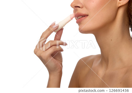 Side view of woman gently using lip balm on upper lip with natural smile, show plump effect and healthy skin against white background 126691436
