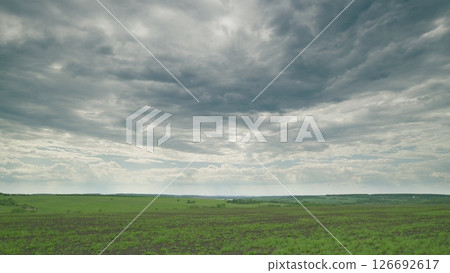 A Serene Overcast Landscape Featuring Expansive Lush Green Fields Under Dramatic Clouds Time lapse. 126692617