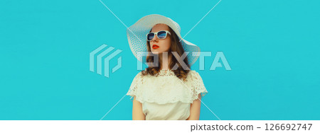 Beautiful stylish young woman in summer white straw hat against blue wall background 126692747