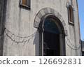Historic Italian church facade with arched doorway, stone details, and string lights casting shadows in sunlight 126692831