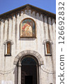 Facade of an old Italian church with a fresco of a saint on horseback above the arched doorway, featuring rustic architecture and religious artwork 126692832