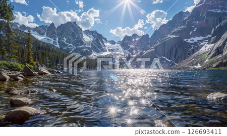 A sparkling alpine lake, encircled by snowy peaks and dense pines, reflects dancing light beneath a vibrant sky. 126693411