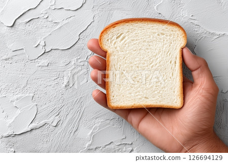 Hand holding slice of white bread on textured background 126694129