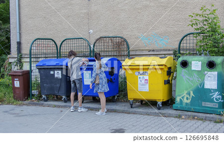 Nitra, Slovakia - 05.21.2025: Young man and woman throwing sorted garbage into different colored bins for collecting materials for recycling. Nitra, Slovakia - 05.21.2025: Young man and woman throwing sorted garbage into different colored bins for collecting materials for recycling. 126695848