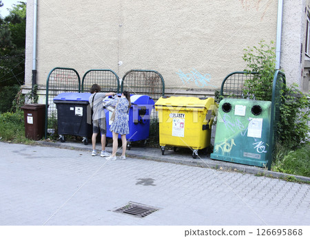 Nitra, Slovakia - 05.21.2025: Young man and woman throw garbage into different colored bins for collecting materials for recycling. 126695868