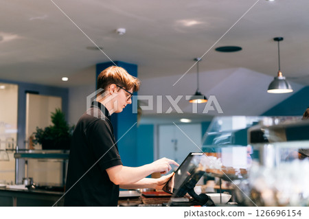 Young waiter serving customer at cash point in cafe. Man working with POS terminal. Student working part-time. Problems of unemployment and Job opportunities for youth. Small business vacancies 126696154