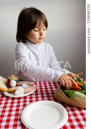 Caucasian child playing with toy fruits and vegetables on red checkered tablecloth 126696339