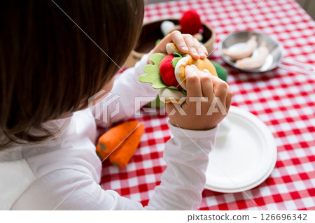 Child engages in imaginative play with toy food at a checkered table Child engages in imaginative play with toy food at a checkered table 126696342