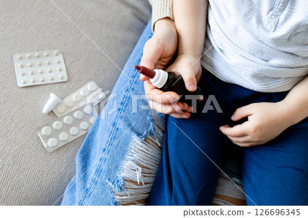 Caucasian young child holding medicine bottle with pills nearby 126696345
