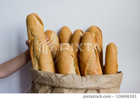Abundance of freshly baked baguettes in brown paper bag with caucasian child hand Abundance of freshly baked baguettes in brown paper bag with caucasian child hand 126696381