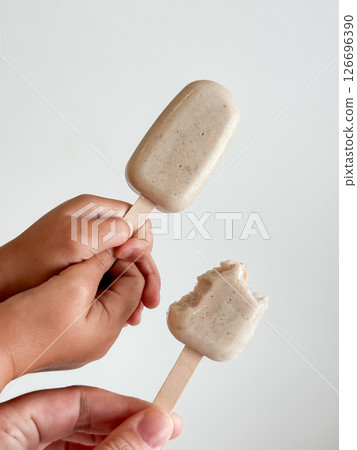 Two hands holding banana ice cream on sticks. Close up with neutral background 126696390