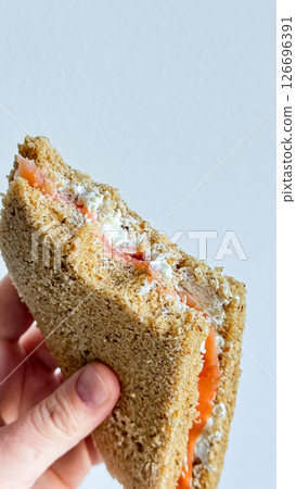 Hand holding salmon and cream cheese sandwich with whole grain bread 126696391