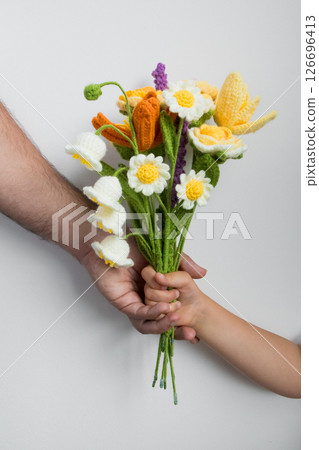 Child hand receiving knitted flower bouquet from adult caucasian male. Fathers day concept 126696413