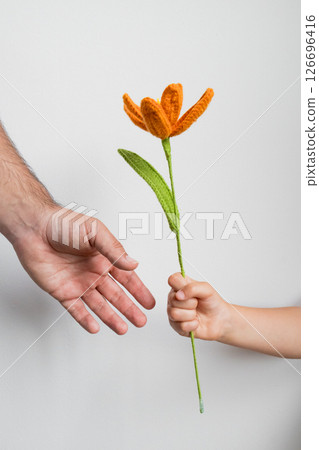 Child giving orange knitted flower to adult hand against white background. Fathers day concept 126696416